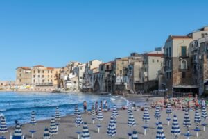Striped parasols on the sand at Cefalu, with the old town built to the water’s edge behind