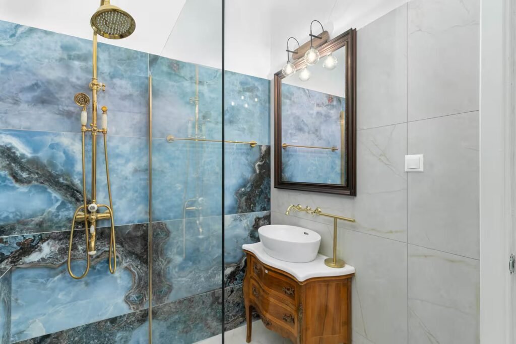 A shower room finished in blue-grey marble with brass fittings, a timber vanity and a framed print above.