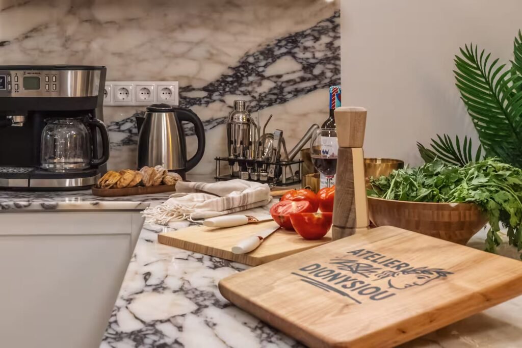 A wooden serving board engraved Atelier Dionysiou, laid on the marble counter with tomatoes and a pepper mill.