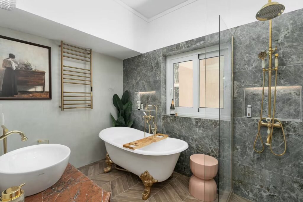 A bathroom lined in green-veined marble, with a clawfoot bath, brass fittings and a heated towel rail.