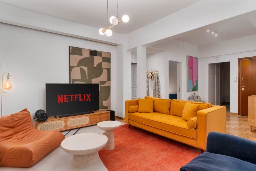 The living room with a mustard sofa, a tan leather lounger, a deep red rug and an abstract canvas above the media unit.