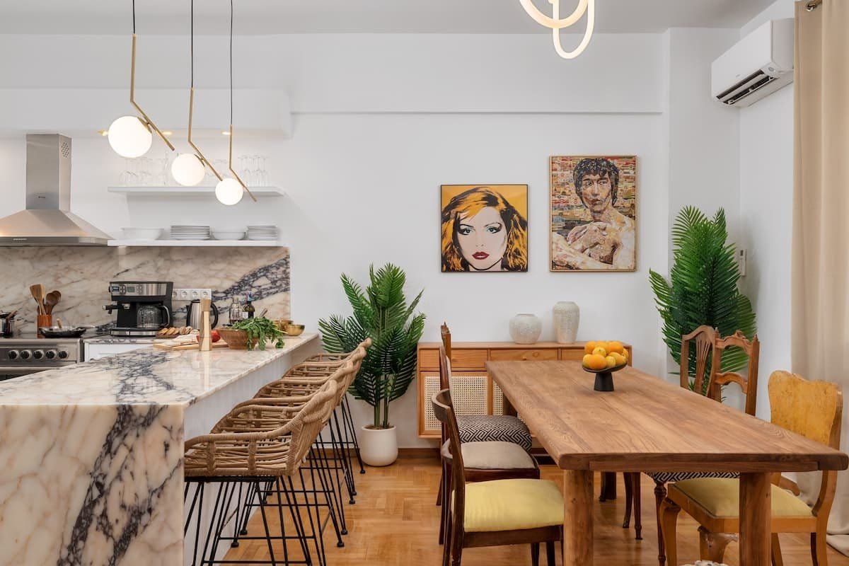 The marble kitchen and dining area, with a veined stone worktop, timber dining table and framed prints on white walls.