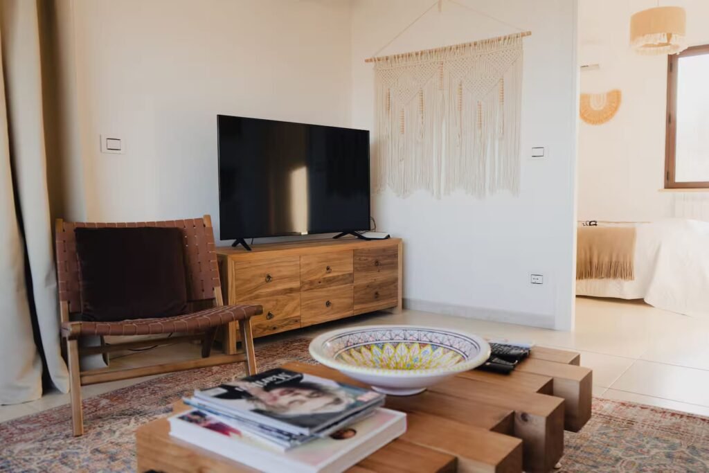 A sitting area with a low timber console, woven wall hangings and a pale rug over parquet.
