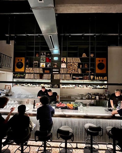A contemporary Athens wine bar, its counter lined with stools and bottles on open shelving.