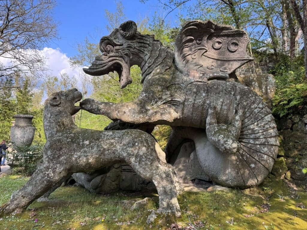 The stone dragon of the Sacro Bosco at Bomarzo, carved mid-struggle with hounds, weathered and moss-covered.