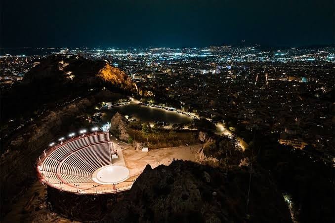 The Odeon of Herodes Atticus lit at night, with the lights of Athens spread out below.