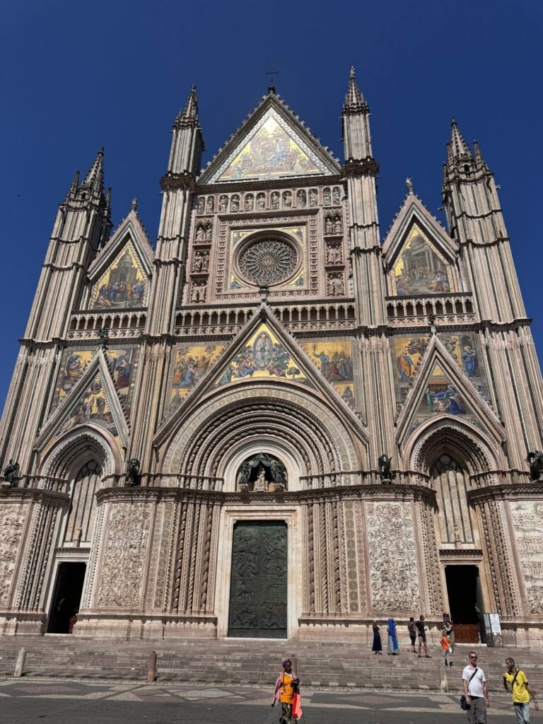 The striped facade of Orvieto Cathedral, its gables set with gold mosaics, seen from the piazza.