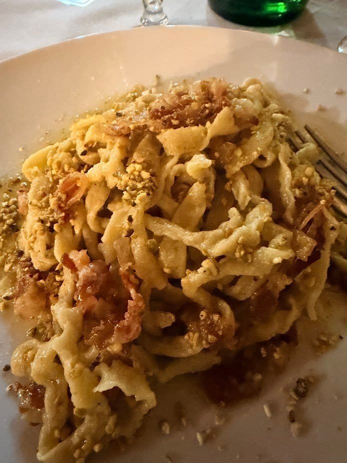 A bowl of pasta finished with grated cheese and black pepper, photographed on a restaurant table.