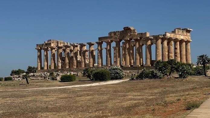 The re-erected columns of a Greek temple at Selinunte, standing on open ground near the sea.