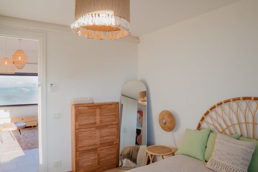 A bedroom with a woven rattan headboard, a tall wardrobe and a doorway through to the terrace.