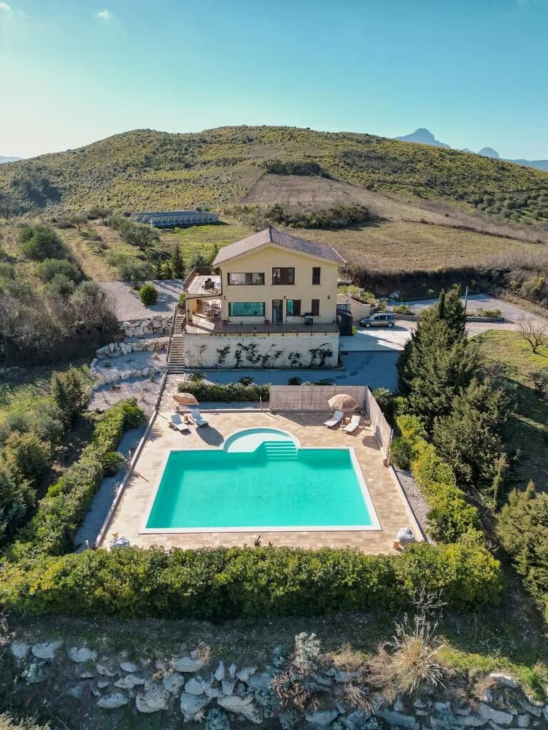 A high aerial view of the villa and pool set within six acres of olive and fruit trees, with the valley beyond.