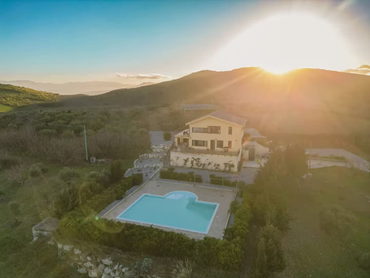 The estate photographed from the air at sunset, the pool catching the last light with the Sicilian hills behind.