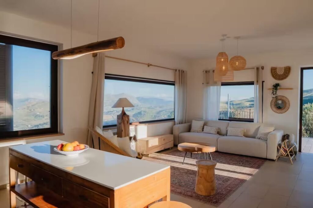 The living room with a pale sectional sofa, woven pendant lamps and a wall of windows framing the mountains.