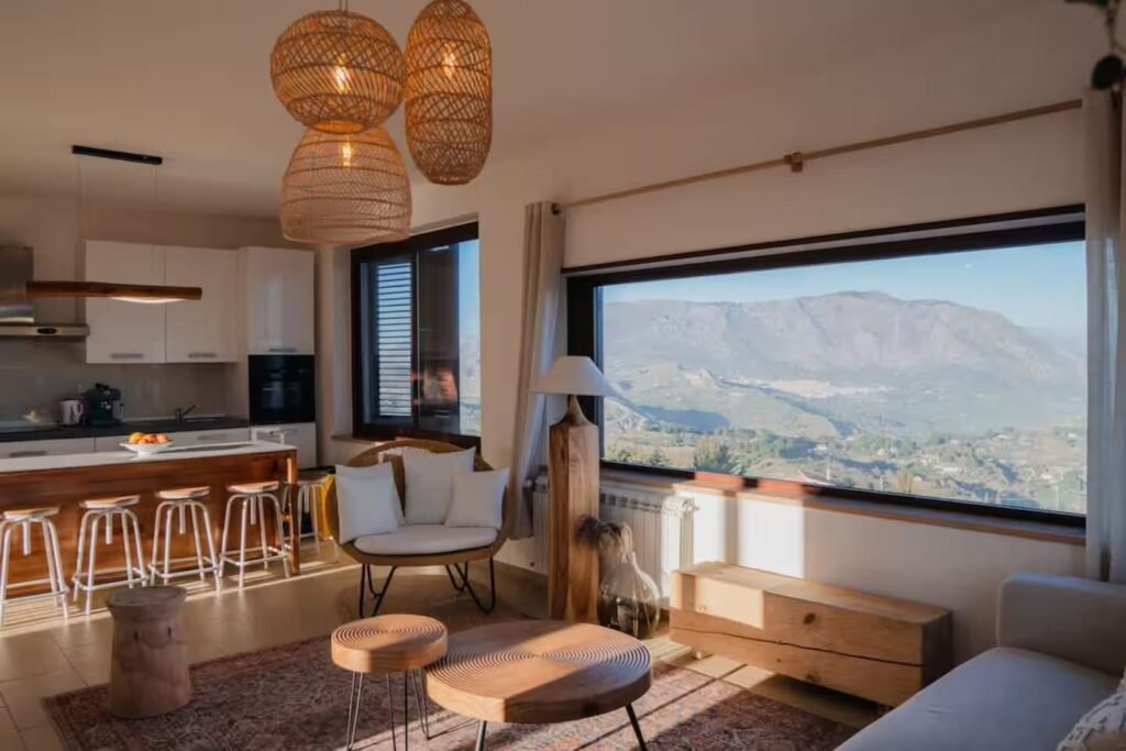 The open-plan kitchen and living space, with bar stools at the counter and a panoramic window onto the mountains.