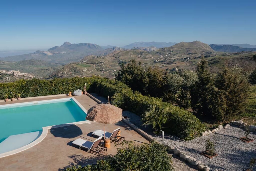 The pool terrace with thatched parasols and loungers, looking out across a wide panorama of mountains and valley.
