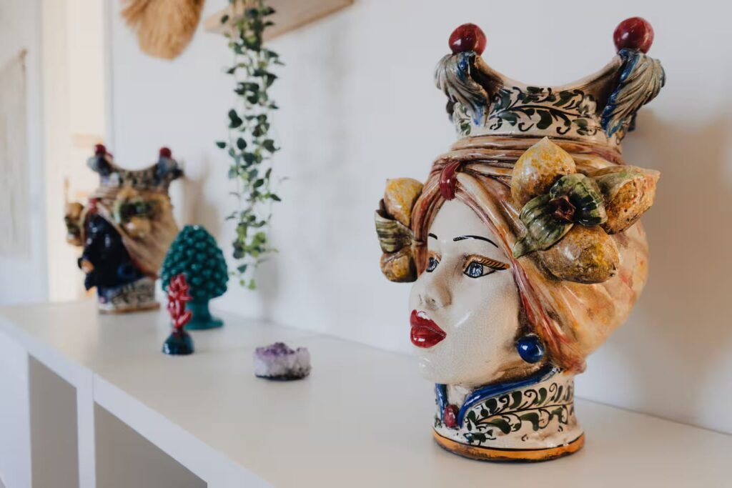A hand-painted Sicilian ceramic head, crowned and glazed in blue and gold, on a white table.
