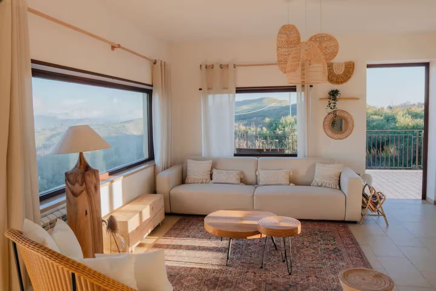 The upper apartment’s living room, with a long sofa, a woven floor lamp and shuttered windows onto the valley.