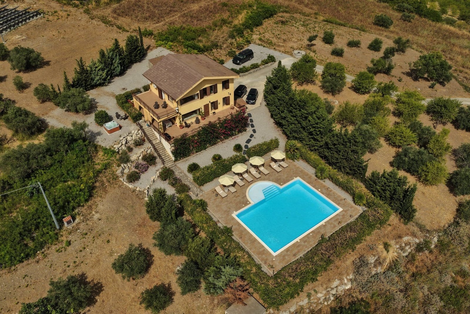 The villa seen from above the private driveway, with parasols and sun loungers arranged along the pool terrace.