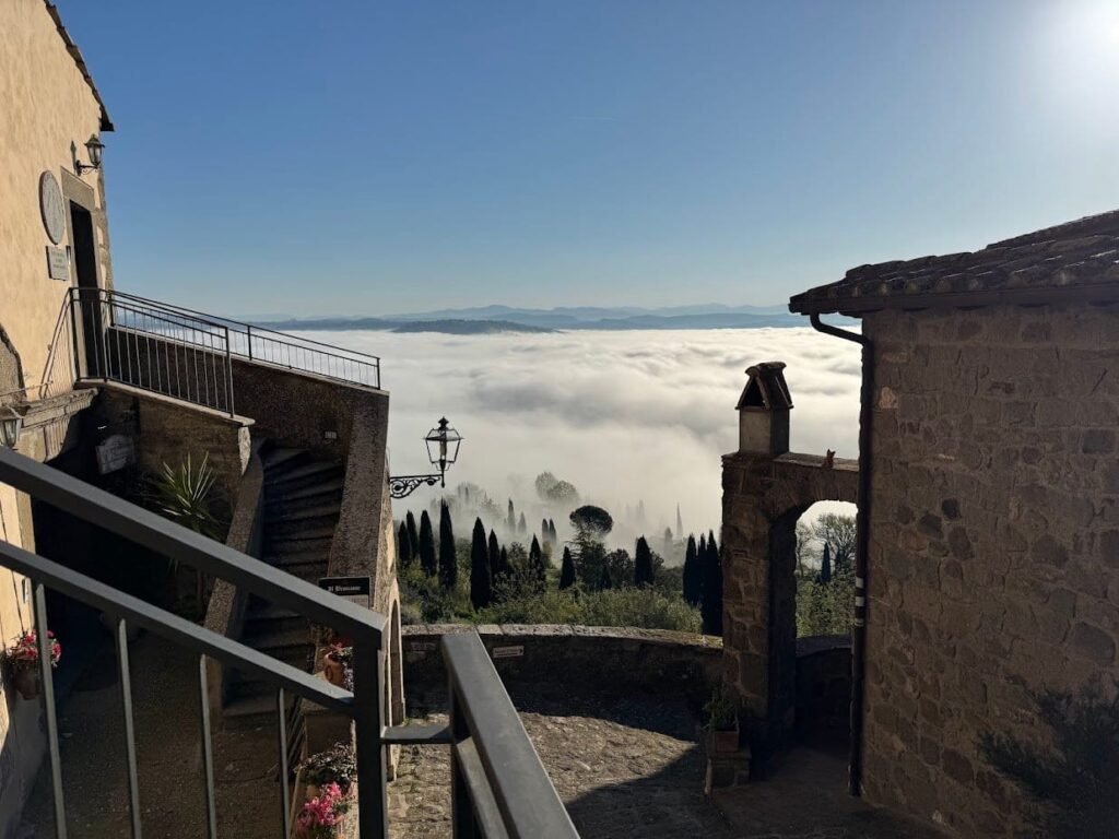 Low cloud filling the Tiber Valley at dawn, seen from the terrace with the village rooftops in silhouette.